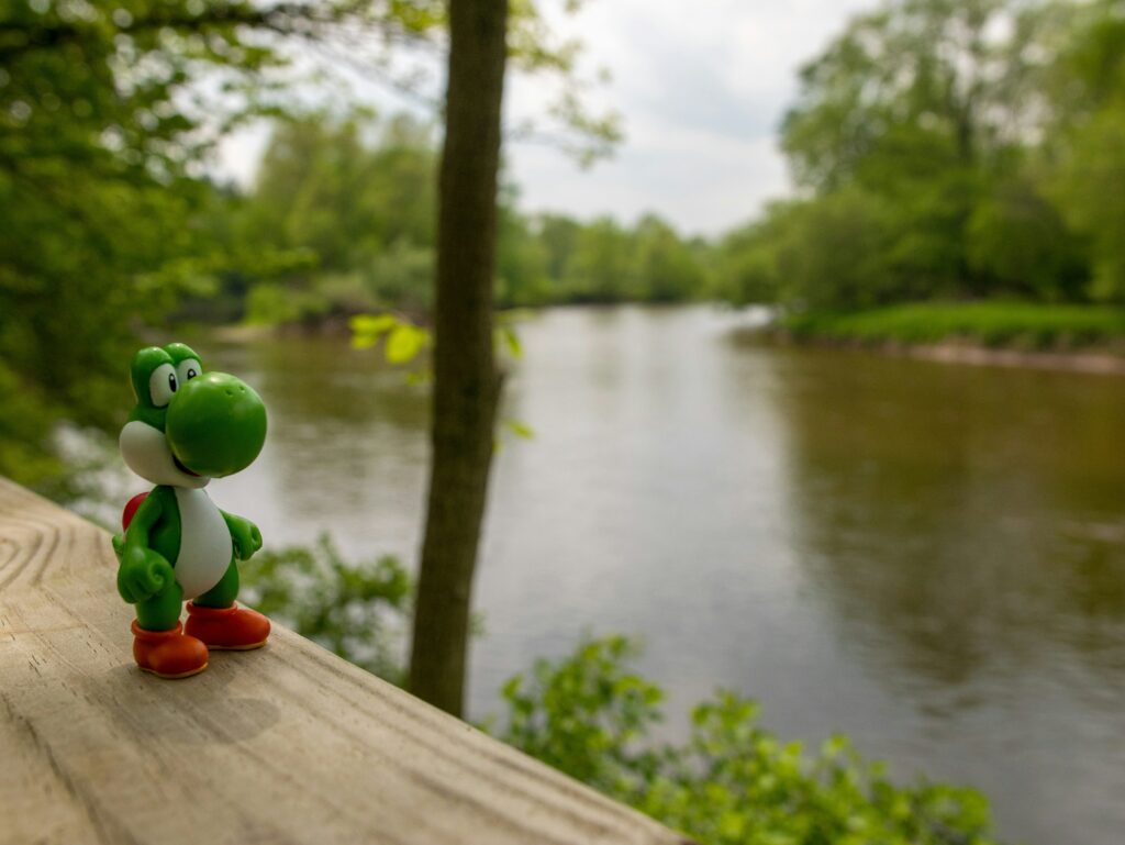plastic figure of Yoshi from Super Mario World on a wooden bench by a pond